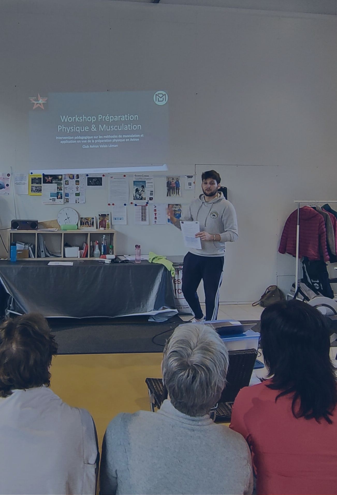 Debout devant une projection, Baptiste Marmoud anime un atelier de préparation physique face à un groupe assis.