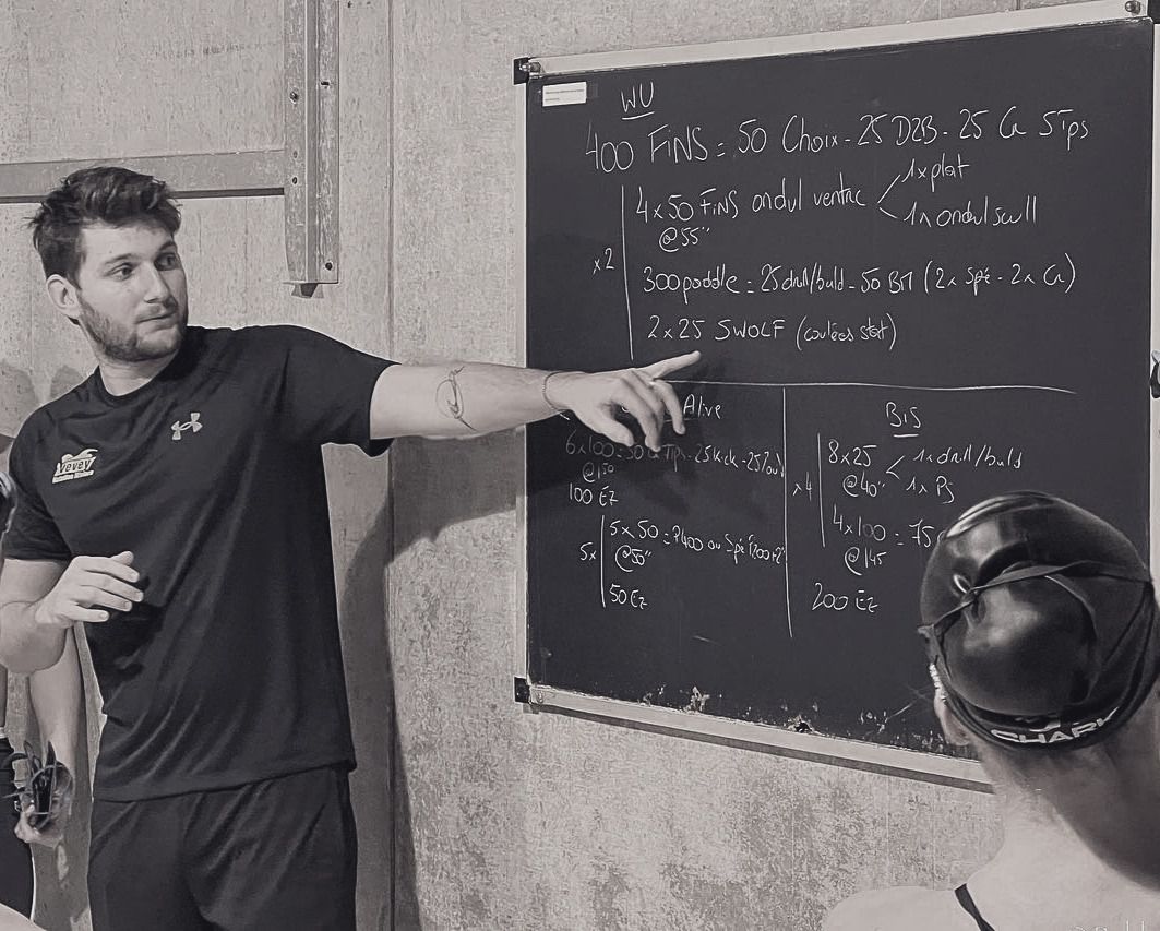 Baptiste Marmoud détaille au tableau noir le plan de la séance de natation, devant un nageur.