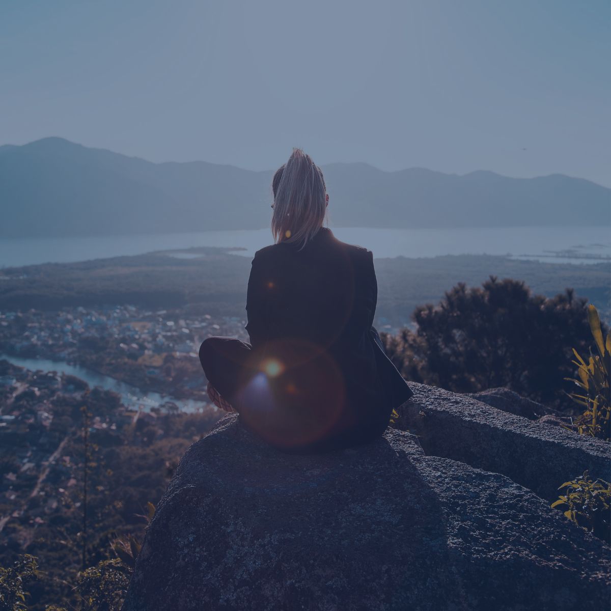 Personne assise sur un rocher face à un lac et des montagnes.